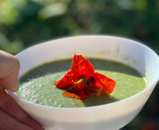 Kom groene soep met een oranje eetbare bloem erop
